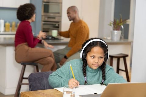 Multiracial parents chatting at kitchen bar while daughter studying on laptop