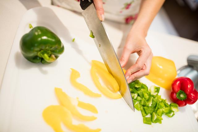 Mid section of woman cutting vegetables on chopping board in kitchen