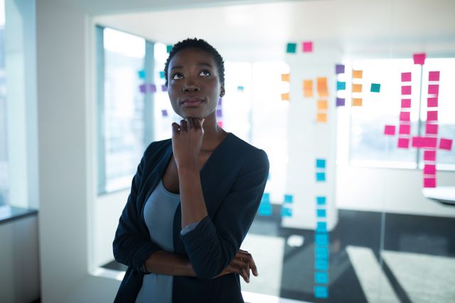 Female executive standing in a modern office, looking thoughtful. Ideal for use in business, corporate, and professional contexts, such as articles on leadership, strategy planning, workplace innovation, and business creativity.