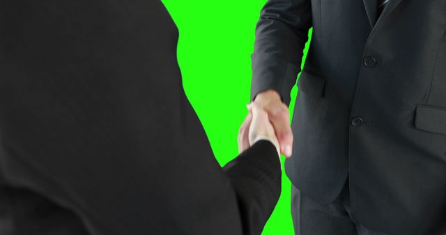 Two businessmen are shaking hands against a green screen background, with copy space. Their handshake signifies a professional agreement or partnership in a corporate setting.