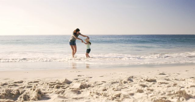 Mother and child joyfully playing on a sandy beach during sunset, waves gently crashing. Perfect for family holidays advertisements, travel brochures, summer vacation promotions, or articles on family bonding and outdoor activities.