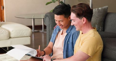 Diverse Gay Couple Celebrating Success at Home with Clipboard