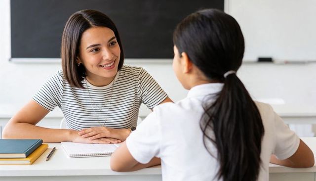 Smiling teacher tutoring student one-on-one at desk with notebooks and chalkboard