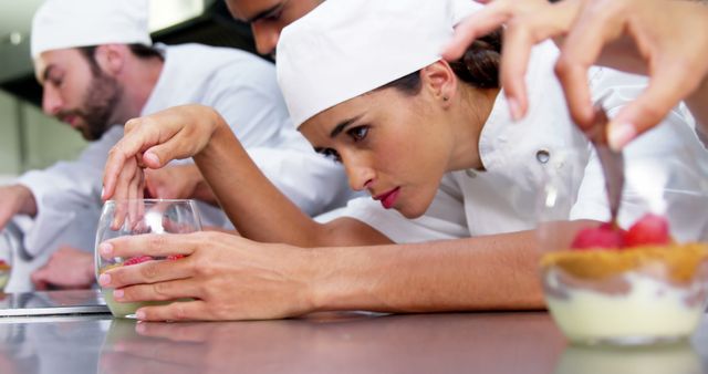 Pastry chefs working together in a professional kitchen, intensely focusing on preparing elaborate desserts. This image is suitable for content related to culinary arts, food preparation, teamwork in the kitchen, or showcasing the skill and dedication of professional chefs. Ideal for use in culinary schools, cooking blogs, or restaurant websites.