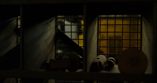 A dimly lit room reveals machinery parts through a barred window, creating a mysterious and industrial atmosphere. The contrasting warm and cool tones add to the intrigue of the setting.