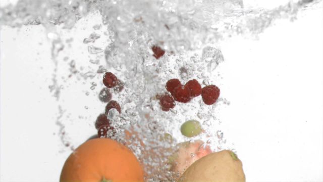 This scene captures fruits including raspberries submerged in water, creating a refreshing splash with visible bubbles against a clean white background. Perfect for websites and advertisements showcasing fresh produce, nutrition, or cleanser products. The dynamic and energetic movement adds appeal for health and wellness campaigns.