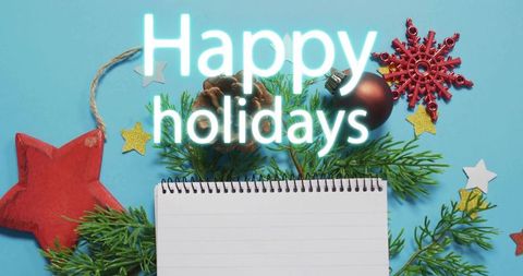 Displaying spiral notebook, holiday greenery and 'happy holidays' neon on blue background