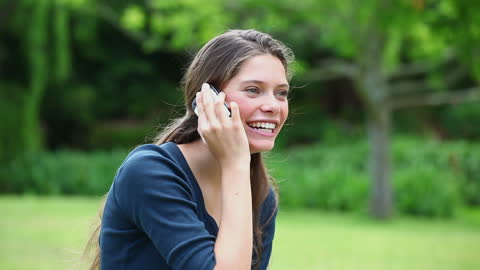 Woman Smiling While Talking on Phone in Lush Green Park
