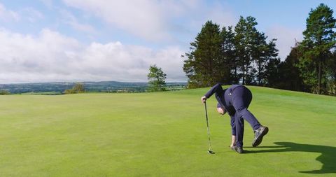 Senior golfer picking golf ball from putting green