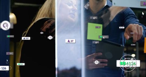 Pointing man guiding colleague at glass while reviewing tablet with analytics overlays