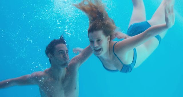 Couple enjoying time together underwater, creating a joyful and playful atmosphere. The image can be used for advertising swimwear, promoting swimming pools, illustrating water activities principles, or highlighting healthy lifestyle and relaxation. It portrays relationship bonding, fun recreational activities, and underwater photography concepts.
