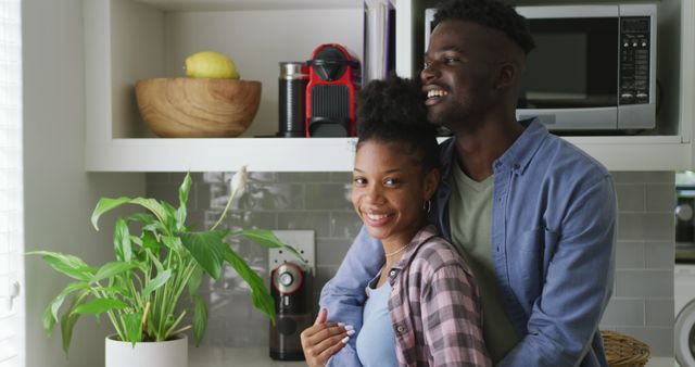 This heartwarming image captures an African American couple in their kitchen, smiling and embracing lovingly. The couple's joyful expression and warm interaction can perfectly represent concepts of love, relationships, and spending quality time at home. Suitable for use in lifestyle blogs, home and relationship articles, advertisements for home products, or promotional materials for relationship counseling services.
