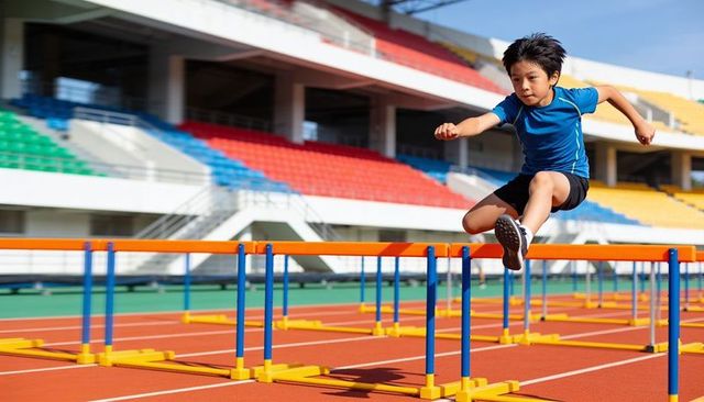 Young asian boy hurdling on red track during youth sprint training in stadium