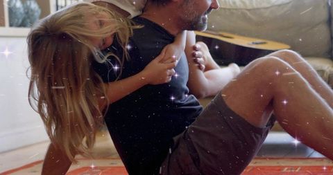 Father playing piggyback with daughter on sunlit living room rug playful family bond