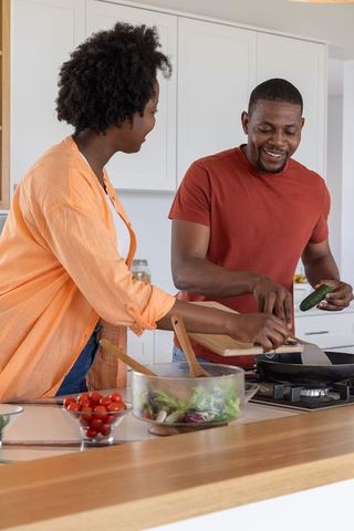 African american couple cooking together in bright modern kitchen preparing fresh salad