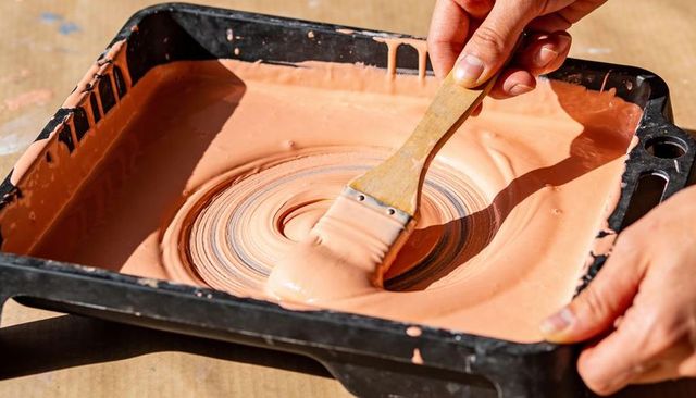 Swirling peach paint with flat brush in tray closeup for diy painting and color mixing