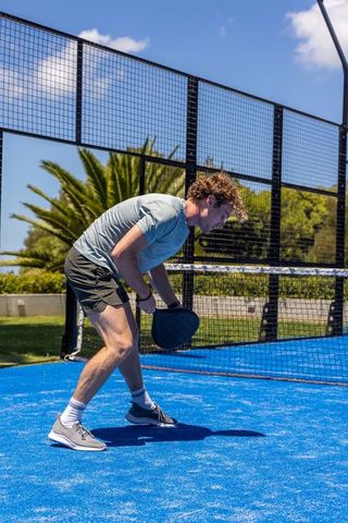 Young man preparing to hit padel shot on vibrant blue outdoor court in sunny sport action