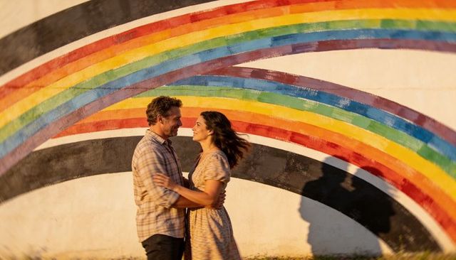 Couple embracing at rainbow mural during golden hour with long shadows
