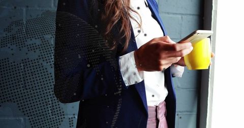 Professional woman engaging with smartphone next to office wall