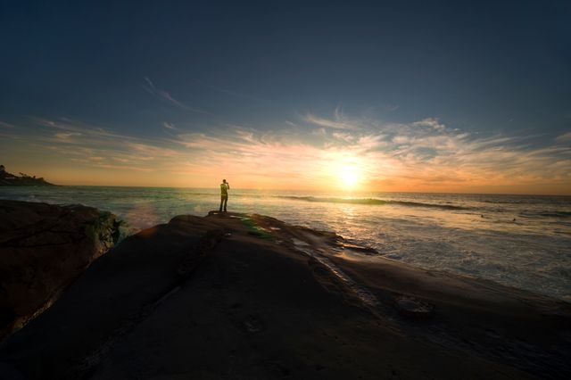 Solitary Figure Watching Sunset on Rocky Beach - Download Free Stock Photos Pikwizard.com