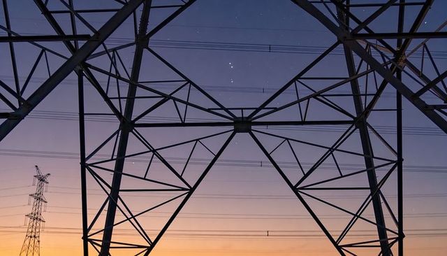 Centering steel lattice transmission tower framing power lines at twilight, gradient sky