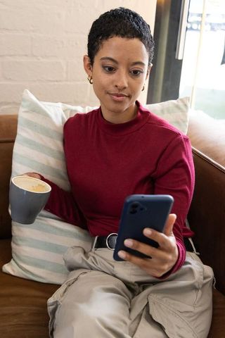 African american woman relaxing on couch holding smartphone and sipping latte in cafe