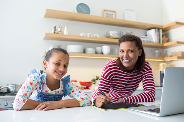Portrait of smiling mother and daughter using graphic tablet in kitchen