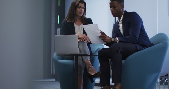 Diverse businessman and businesswoman discussing documents and using laptop in modern office. business and business people in office concept.