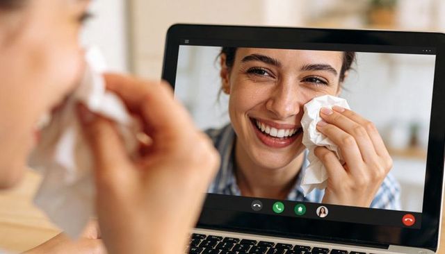 Smiling woman wiping tears during emotional laptop video call, offering remote comfort