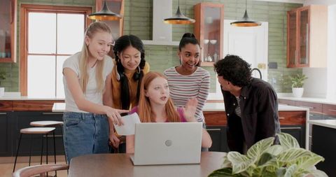 Multicultural Teen Team Collaborating Around Laptop for School Project in Modern Kitchen