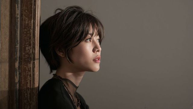 Contemplative asian woman leaning on worn wooden frame with moody sidelight portrait minimal