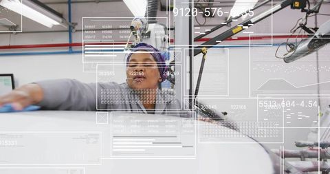 Technician wiping curved panel in industrial workshop with ar interface and overhead crane