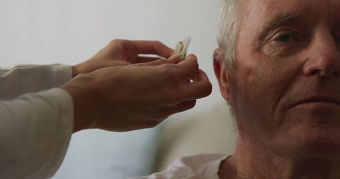 Senior man receiving hearing aid from caregiver at home