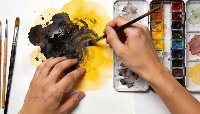Artist hands painting bold yellow black watercolor circle with palette and brushes
