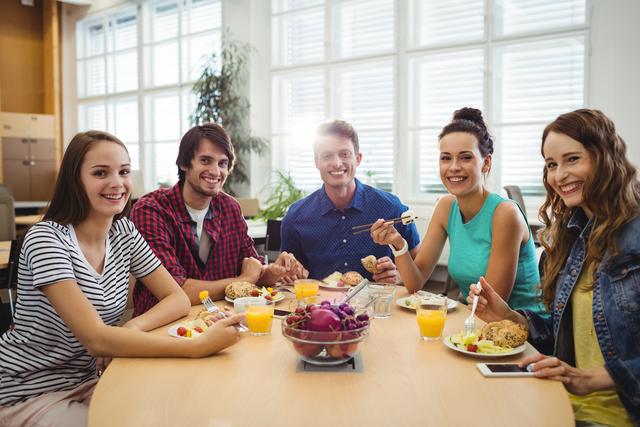 Group of business executives enjoying a meal together in an office setting. They are smiling and appear to be having a good time, suggesting a positive work environment. Ideal for use in articles or advertisements about workplace culture, team building, corporate events, or healthy office habits.