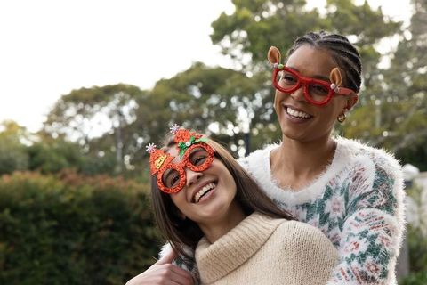 African american and asian friends wearing festive glasses and cozy knits laughing outdoors