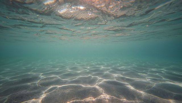 Turquoise seabed with rippled sand and sunlight caustic patterns tranquil background