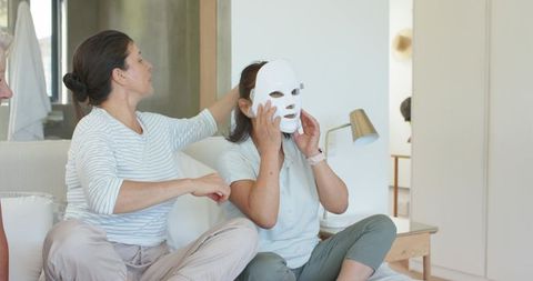Senior friend adjusting led facial mask during home skincare routine with companion