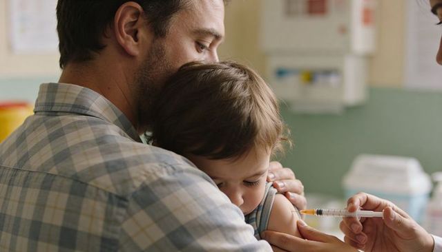 Father holding toddler while nurse giving vaccine, comforting pediatric immunization scene