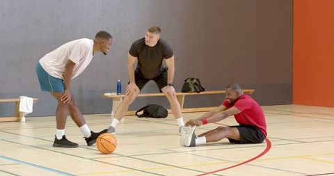Diverse male teammates stretching and preparing for basketball drills on indoor gym court