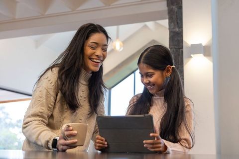 Mother and daughter smiling and bonding while using tablet at kitchen counter