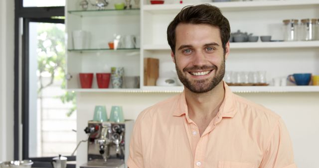 Happy caucasian man with beard standing in kitchen and smiling in sunny home. Lifestyle, free time, wellbeing and domestic life, unaltered.