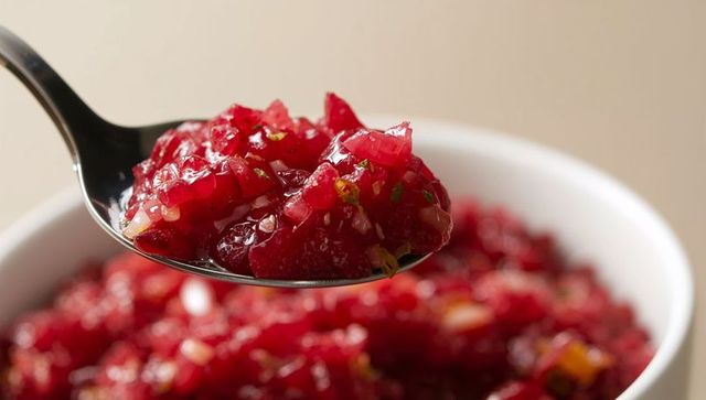 Spoon scooping glossy cranberry relish with herbs and onion over white bowl seasonal menu