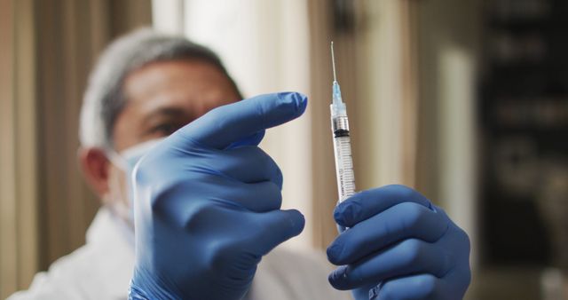 Healthcare worker wearing blue gloves and mask, holding and preparing a syringe with vaccine injection. Ideal for content on medical procedures, vaccination drives, healthcare industry, hospital settings, and promoting immunization awareness.