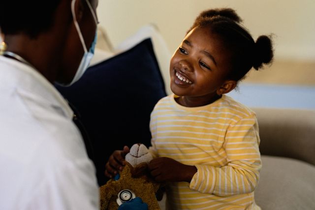Smiling african american girl having medical visit with doctor wearing face mask. healthcare and medicine during coronavirus covid 19 pandemic.