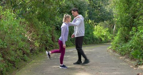 Couple stretching on forest trail, man steadying woman during standing quadriceps stretch