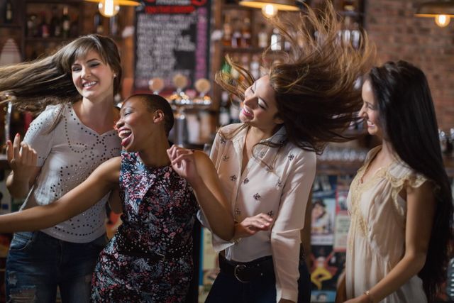 Group of female friends enjoying a night out at a pub, dancing and having fun. Perfect for use in advertisements for nightlife, social events, friendship, and youth culture. Can also be used in articles or blogs about socializing, celebrations, and enjoying life.