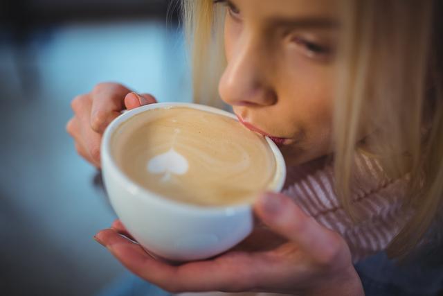 Woman enjoying a hot cup of coffee with heart-shaped latte art, perfect for illustrating concepts of relaxation in a cafe, enjoying warm beverages, and leisurely mornings. Useful for promoting cafes, coffee brands, lifestyle blogs, and morning routine themes.