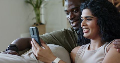 Young couple relaxing on sofa, browsing flip phone and sharing cozy home lifestyle moment