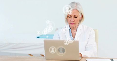Senior female doctor typing on laptop updating electronic patient records in modern clinic